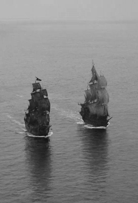 a high angle view depicts two sailing vessels navigating through the ocean in black and white.