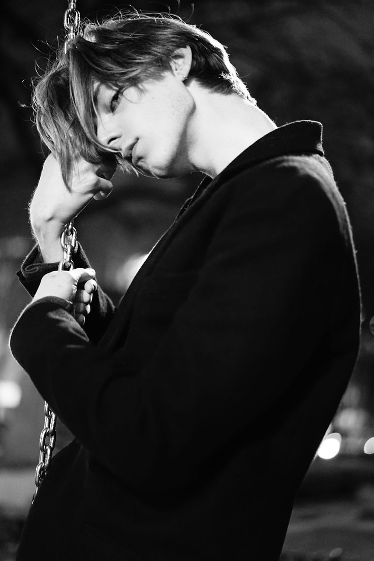 a black and white portrait of a young man wearing a jacket,  with a chain hanging from his jacket.  the man has a serious expression and appears to be lost in thought.