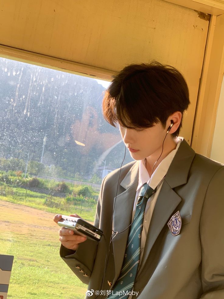 a young man in a school uniform stands by a train window, bathed in warm, golden hour sunlight.  he's looking down at a vintage music player in his hands, headphones in his ears, seemingly lost in the music and the passing scenery. the atmosphere is peaceful and nostalgic.