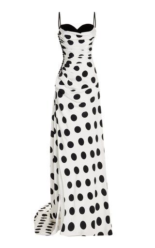 a white maxi dress with black polka dots. the dress has spaghetti straps, a bustier top, a draped bodice, and a ruched skirt.