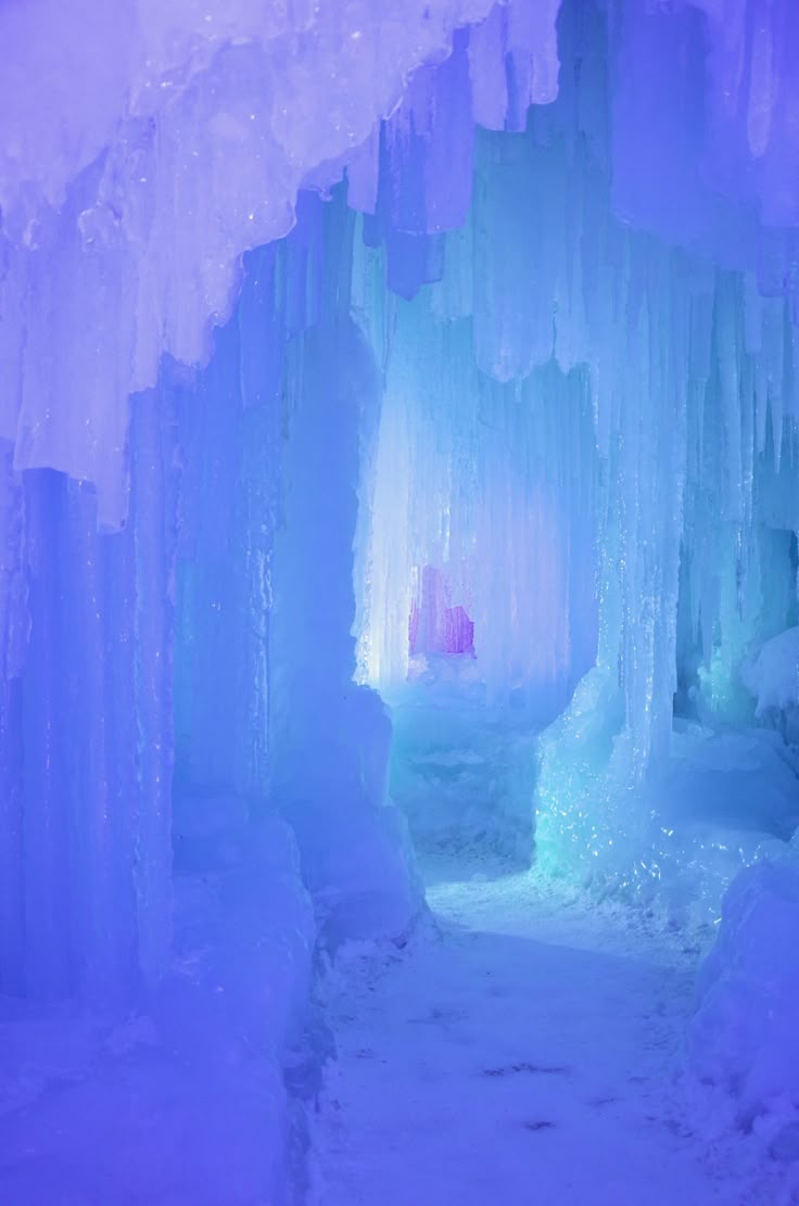 this is an image of an ice castle. the structure is made of blue and purple ice and icicles. a passageway leads through the castle. the scene is indoors and evokes a wintery atmosphere.