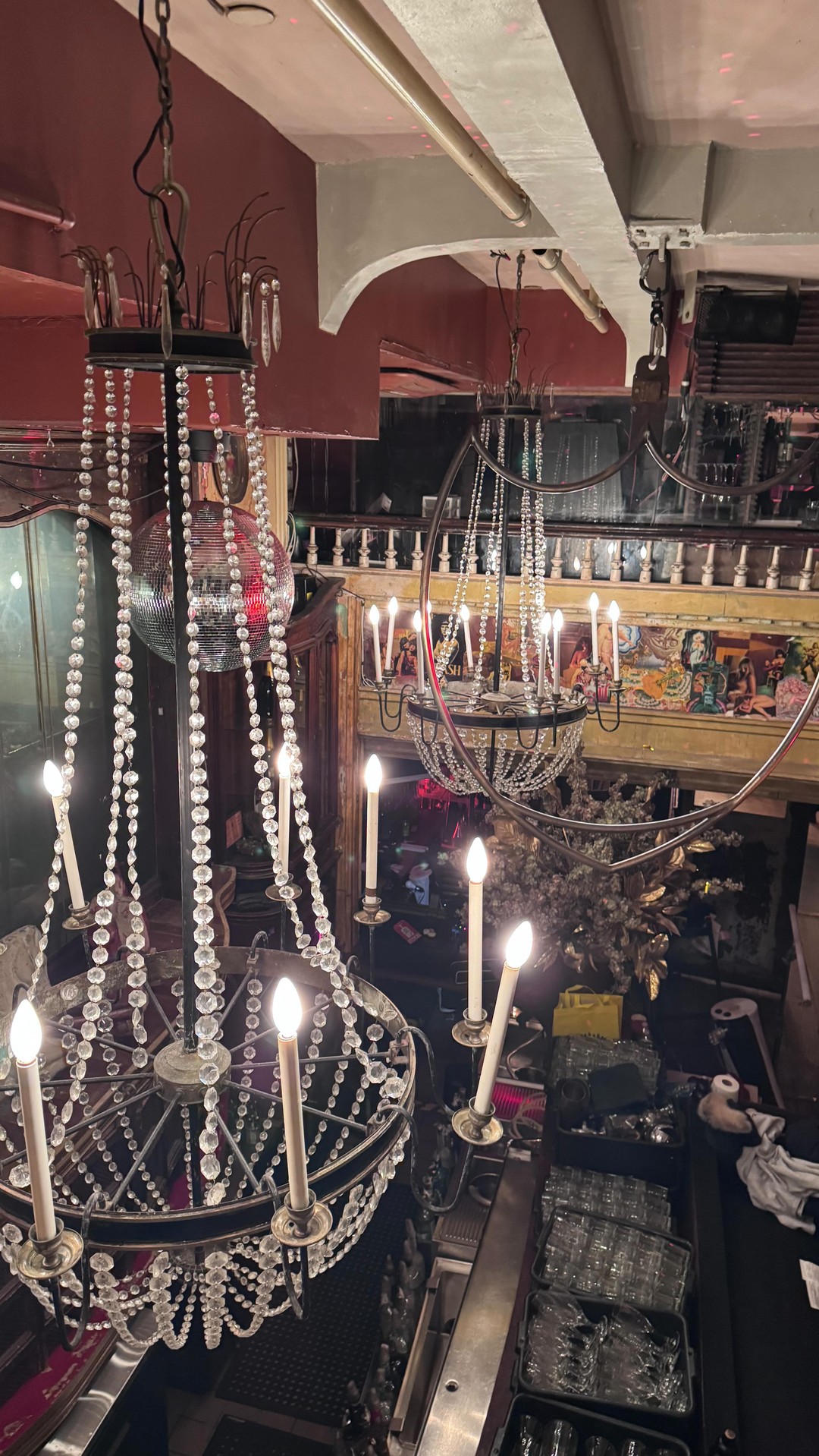 this photo shows a decorative interior with multiple chandeliers and a disco ball. there are light fixtures hanging in the space, and there is architecture that gives a sense of a restaurant or bar setting.