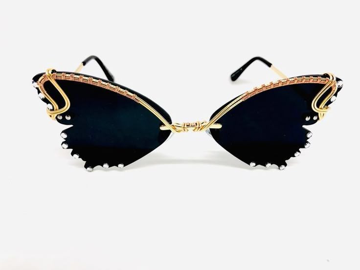 the image showcases a pair of butterflyshaped sunglasses with black lenses, intricately decorated with gold and copper wire around the frames, and adorned with small, clear jewels along the edges of the lenses. the design gives the eyewear a unique, handcrafted, and fashionable appearance.