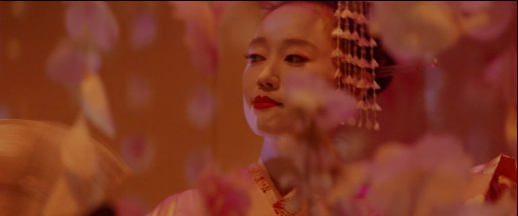 a closeup portrait of a geisha, her face framed by delicate, outoffocus cherry blossom decorations. she is adorned in traditional white makeup, vibrant red lipstick, and a pink kimono. the warm, soft lighting and shallow depth of field emphasize her serene beauty and the elegance of her cultural attire.