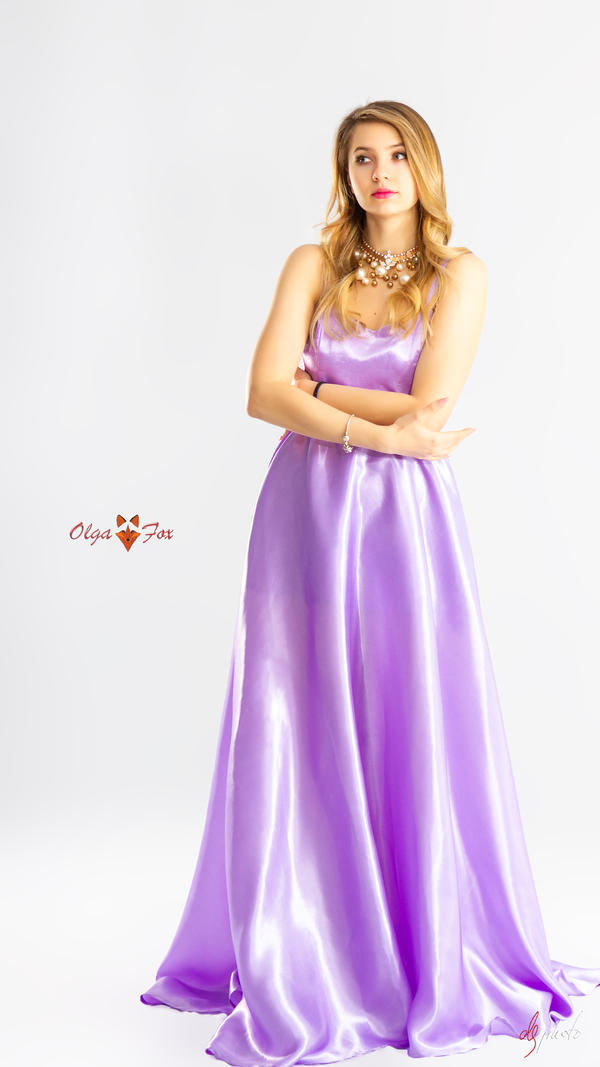 a fulllength studio shot of a beautiful blonde woman in a flowing lilac satin maxi dress. she has her arms crossed and is looking off to the side with a thoughtful expression.  the dress is sleeveless and features a simple, elegant design. she is wearing a pearl and gold necklace. the background is plain white, allowing the dress and the model to be the focal point. the image has a sophisticated and elegant feel.