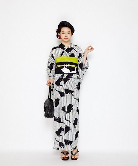 a full shot of a young woman dressed in a catpatterned kimono. she is wearing a black beret and sandals, and carrying a black handbag. the kimono is white with black vertical stripes and black cat silhouettes, complemented by a vibrant yellow obi. the background is plain white.
