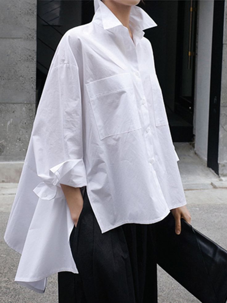 a woman is wearing an oversized white shirt that has been styled with a black skirt, creating a casual and chic look. the shirt is loose and flowy, giving the outfit a relaxed feel. she is standing on the street with her arms at her sides, and the shirt is hanging off her body in a stylish and carefree way.