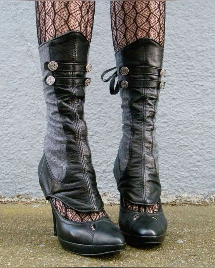 the image shows a closeup view of a pair of unique, custommade women's boots. the boots are a blend of styles: the upper portion seems to be constructed from a gray fabric, while the lower portion and high heels are made of black leather.  they feature several details suggestive of steampunk or victorianinspired fashion:  metal decorative buttons are fastened along the shaft, and the boots are worn over black fishnet stockings. the boots are highheeled, pointedtoe style, and appear to be handcrafted or custommade. the overall aesthetic is dark, elegant, and slightly gothic.  the boots are standing on a light gray concrete surface against a textured gray wall.