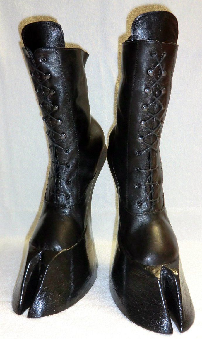 a pair of black, kneehigh, laceup leather boots with a hoofshaped toe stand upright against a white backdrop.
