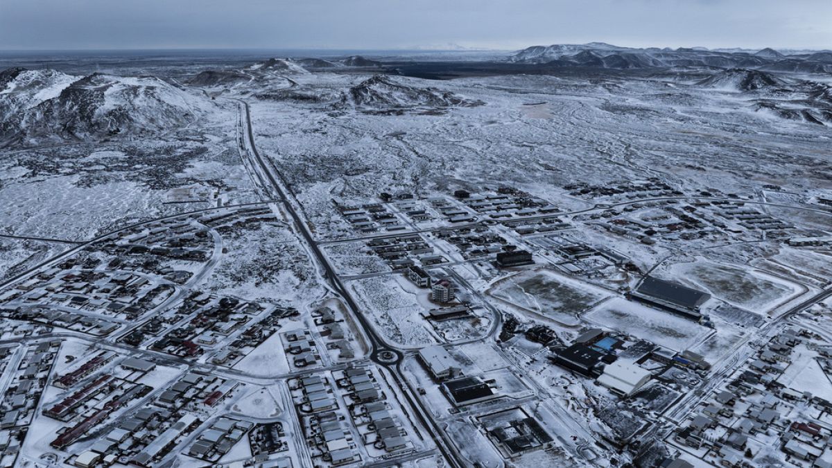 an aerial view of a town in iceland during the winter. the town is covered in snow, and the buildings are clustered together. the streets are narrow and winding. the horizon is in the background and is dominated by a snowy mountain range. the sky is overcast and the snowcovered landscape stretches out to the horizon.