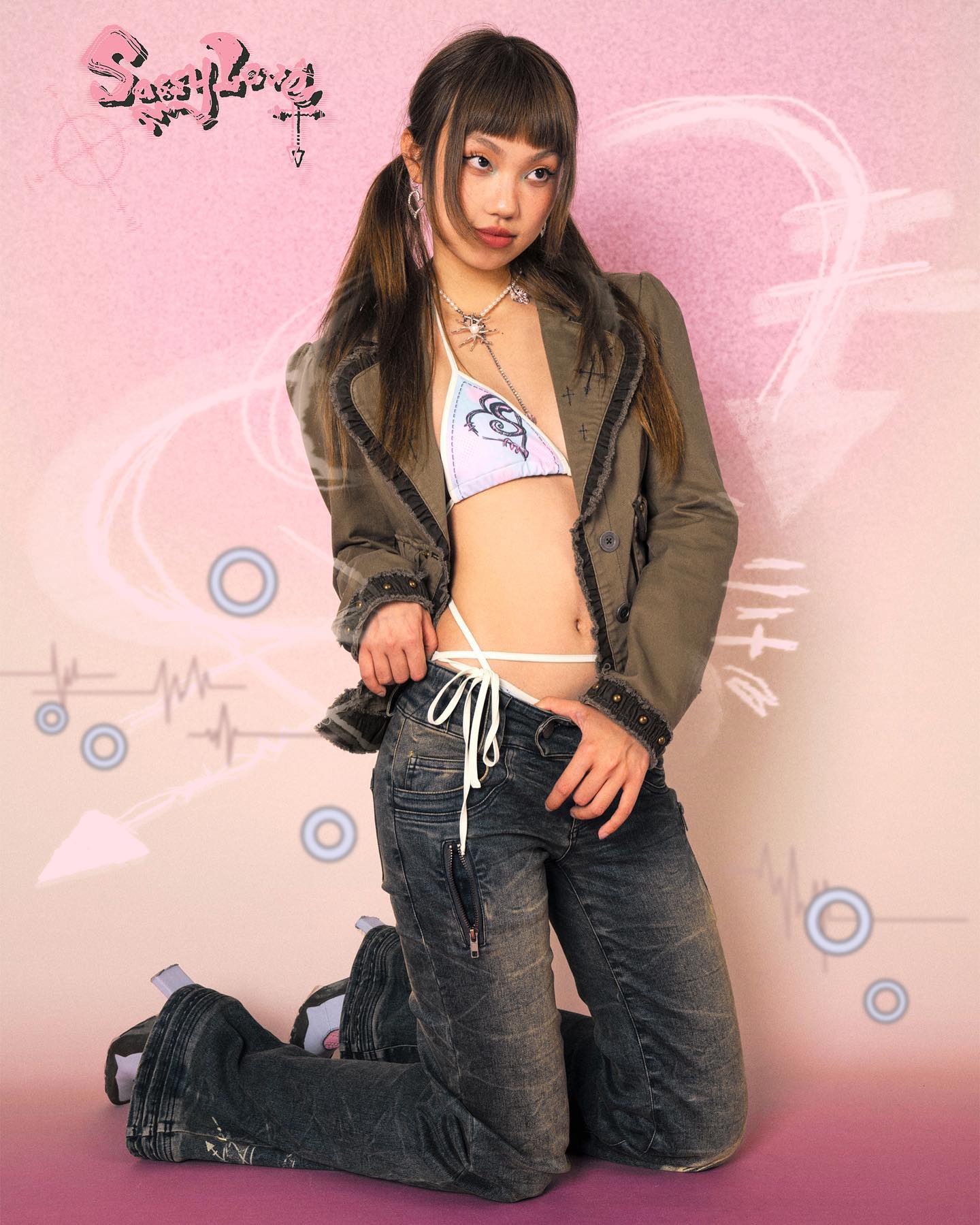 the image showcases a young female model in a stylish photoshoot. she is kneeling on a pink background adorned with abstract graphic elements. the model is dressed in lowrise distressed bellbottom jeans, an olivegreen jacket, and a lightcolored bikini top featuring a heart design.  she also wears a delicate necklace. her hair is styled in pigtails, completing a y2k or sweetgrunge inspired look. the overall aesthetic is a blend of vintage, grunge, and kawaii elements.  the brand name "suzy love" is prominently displayed, suggesting a potential promotional image for a clothing line or brand.
