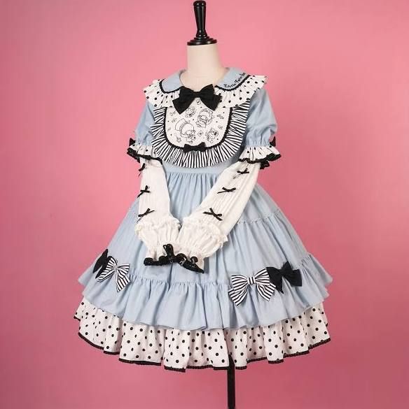 a baby blue lolita fashion dress with white polka dots, black ribbon accents, and a white peter pan collar with black trim is shown on a mannequin against a solid pink background. the dress is short, with a tiered skirt and puffy sleeves. the bodice features a print and lace trim.  the lighting is soft, and the perspective is at eye level.
