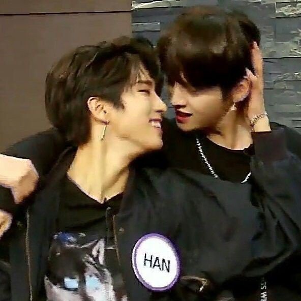 two men are hugging each other. the one on the left is wearing a black jacket over a white shirt and has short black hair. the one on the right has longer dark hair and is wearing a black shirt. the one on the right is holding the other one by his hair.  the man on the right has a name tag that says "han" on it.  they both have very serious expressions on their faces and they both seem to be enjoying each other's company.