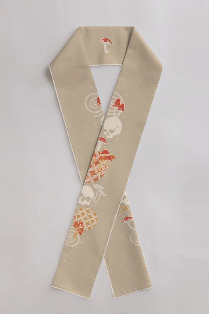 a tan scarf with a white border features a pattern of mushrooms, skulls, and swirling designs.