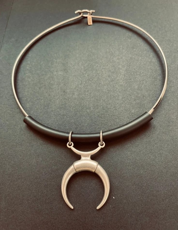 a silver choker necklace with a black rubber band and a silver crescent moon pendant. the necklace is on a dark background.