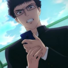 a young man with short black hair and glasses, wearing a black shirt, is shown in a closeup, outdoor setting. he appears upset as he looks down at a dark blue smartphone in his hands, with his mouth slightly open, as if in frustration.  the background features a bright blue sky with some white clouds, along with a glimpse of green fencing, creating a stark contrast to his expression.