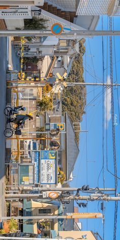 the image shows a busy street scene in japan, viewed from a high angle. the sun is shining brightly, illuminating the buildings and the street below. there are numerous signs in japanese, adding to the sense of place. a cyclist can be seen riding on the left side of the road, seemingly heading towards the camera. the overall impression is of a bustling and vibrant city.