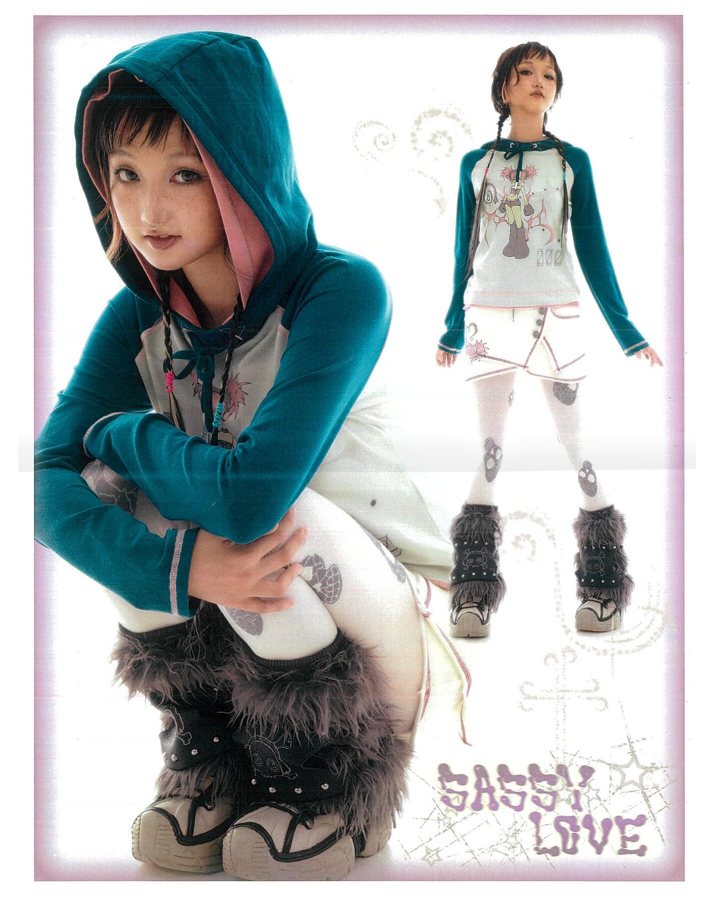 he image shows two shots of a young woman modeling different outfits.  the main focus is on a girl wearing a teal hoodie with a pink interior, white tights with skull designs, and fluffy grey leg warmers with black boots. she is sitting with her legs tucked under her. in the background, there's a smaller image of the same model wearing a white top with a cartoon design, a white skirt, and similar leg warmers and boots.  both outfits are in a style that blends elements of kawaii, lolita, and punk aesthetics.  the background is light and features whimsical designs. the overall feel is youthful and stylish.