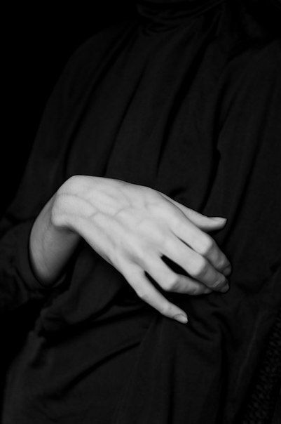 a person wearing a black turtleneck shirt is shown with their hand resting on their chest. the image is black and white.