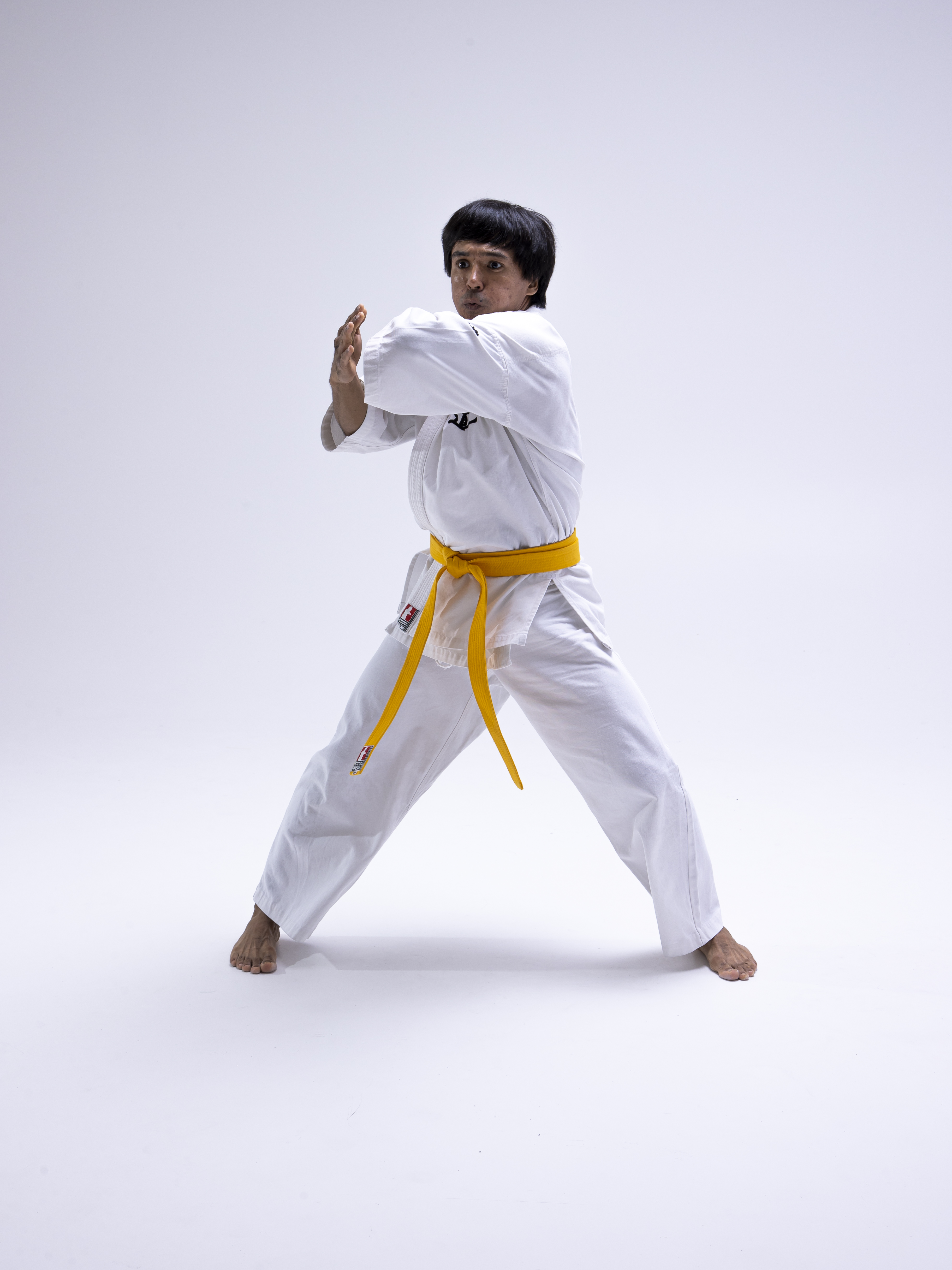 a man wearing a white karate uniform with a yellow belt is in a stance against a white background.
