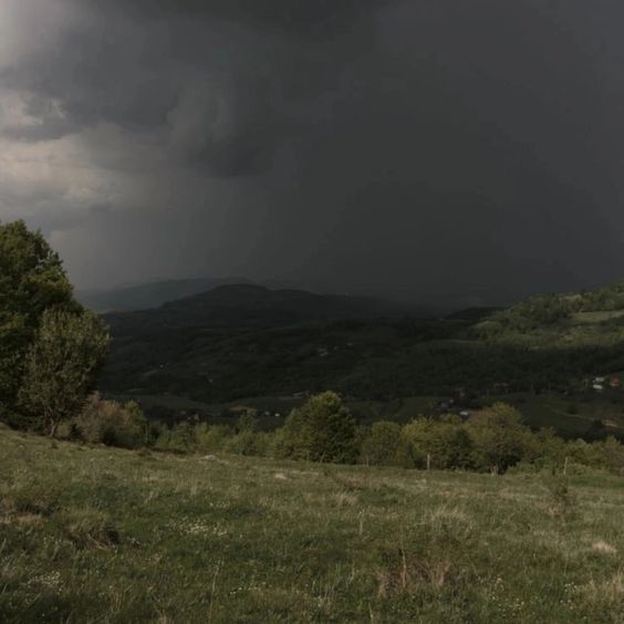 a lush green landscape stretches beneath a brooding sky heavy with dark storm clouds.  the hills roll into the distance, their details obscured by the approaching weather. the light is subdued, creating a sense of drama and anticipation.