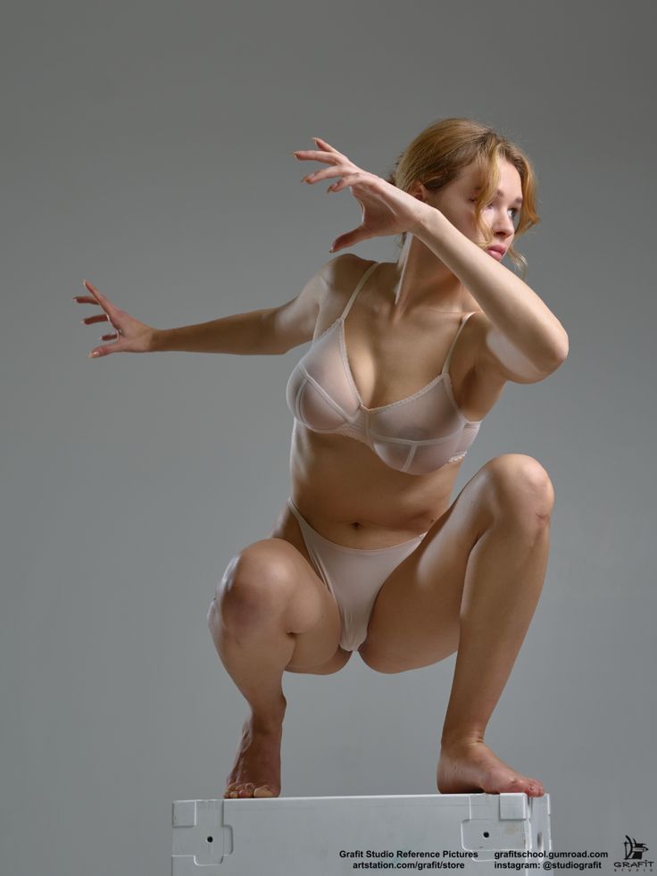 a slender, caucasian woman is crouching on a white platform in a studio setting with a neutral gray background. she is wearing a translucent bra and panty set, showcasing her pale skin. her bare feet are planted on the platform, and she is in a dynamic pose with one hand outstretched towards the left and the other arm bent across her face, obscuring part of her view. she is looking away with an air of elegance and sensuality. the image is a studio shot, focused on the model in an artistic pose.