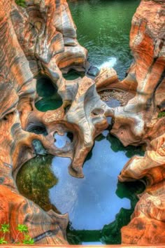a stunning aerial view of a canyon with intricate rock formations and pools of water. the weathered rock is a mixture of browns, oranges, and reds, creating a captivating abstract pattern. the blue and green water reflects the sky and surrounding vegetation, adding a touch of serenity to this rugged landscape. this image captures the beauty and power of nature's artistry in shaping the earth's surface.