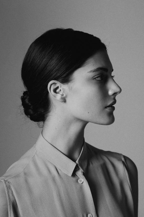 a black and white portrait of a woman in profile, with her hair pulled back in a bun and wearing a collared shirt.