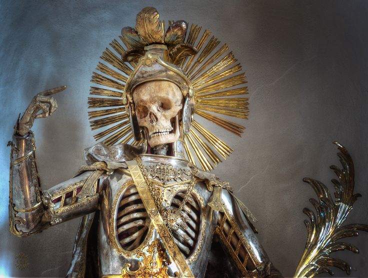 a closeup of a skeleton wearing a suit of armor and a golden crown, with a golden halo. it's an intricate and detailed sculpture, with the skeletal structure intricately rendered and the armor ornamented with intricate details. the sculpture has a gothic and medieval aesthetic, with a macabre and grim reaper quality. it's a powerful and evocative piece of art, reflecting on death and mortality. the artwork may be found in a church or religious setting, serving as a reminder of the fleeting nature of life.