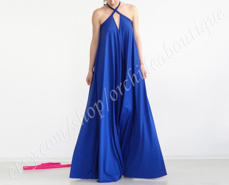 a woman is wearing a long, blue halter neck maxi dress. the dress is a vibrant blue and features a halter neckline with a small cutout in the front. the dress is flowing and loosefitting. the woman is standing in front of a white background. there is a pink strap lying on the floor to the left of the dress.