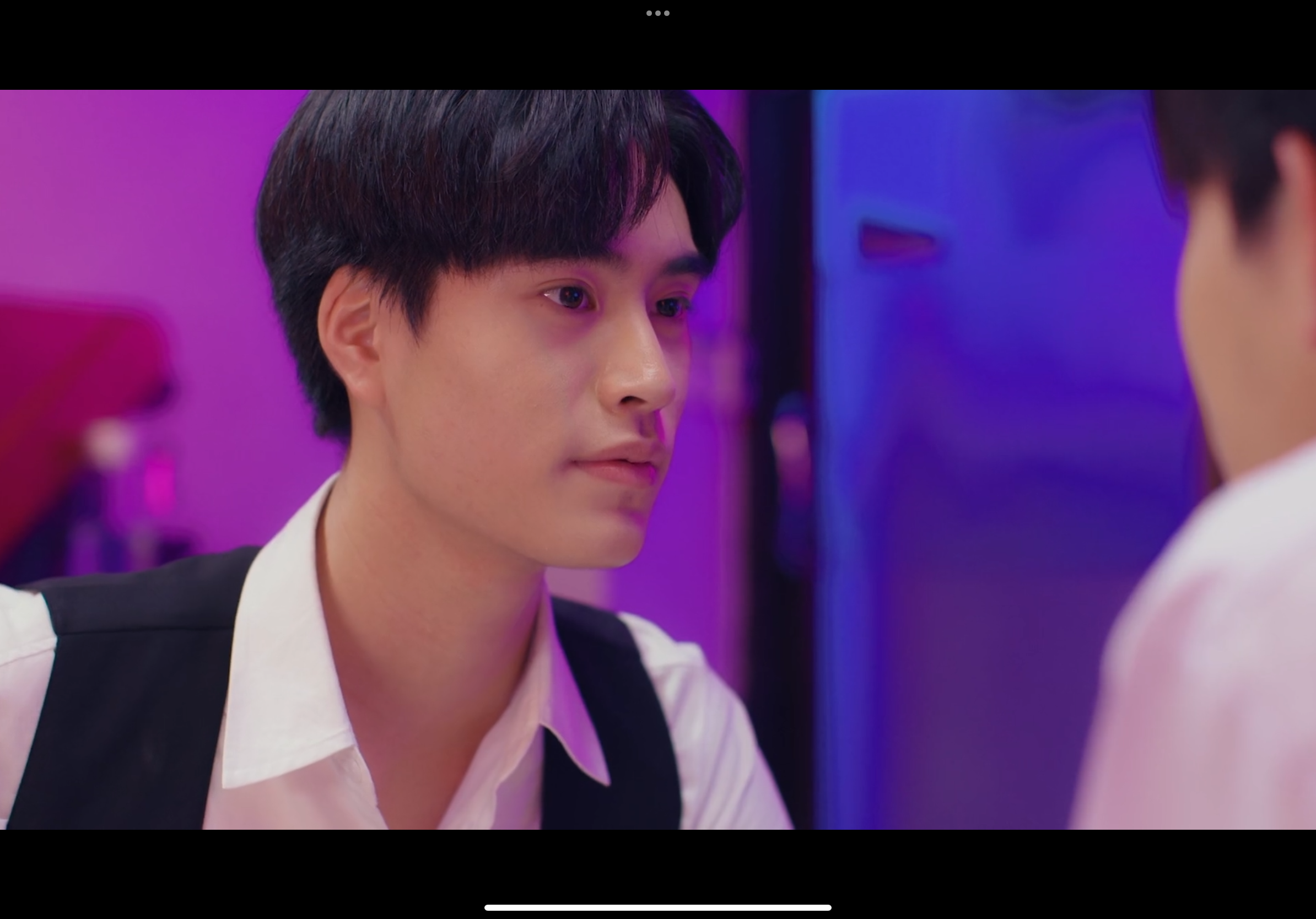 two young asian men gaze intently at each other in a dimly lit room with pink and blue lighting. the focus is on the man in the foreground, his expression serious and filled with unspoken emotions. the man in the background is out of focus, his features blurred. the atmosphere is charged with a sense of intimacy and anticipation.