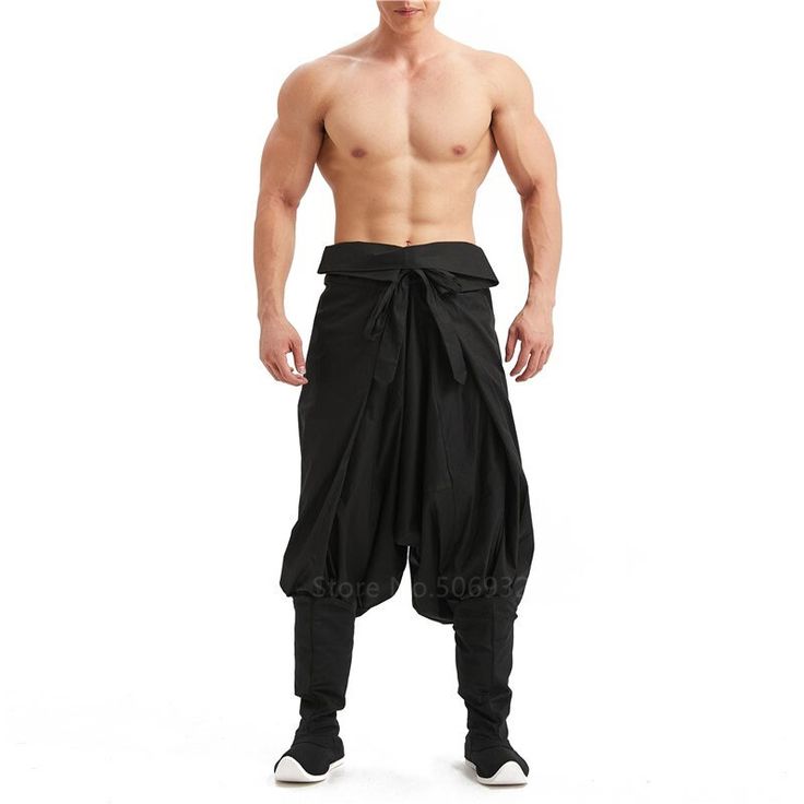 a man is wearing black hakama pants. the pants are loosefitting and flowy, and they have a wide waistband with a sash. the man is standing with his legs apart, and he is looking at the camera. the pants are made of a lightweight fabric that is comfortable to wear. the man is wearing a pair of white sneakers.