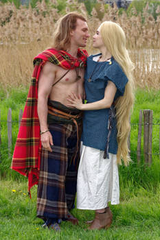 a man and a woman, dressed in traditional scottish attire, stand embraced in a grassy field. the man wears a kilt and plaid, while the woman wears a long, flowing dress. the scene is set outdoors, with tall reeds in the background.  they appear to be romantically involved, looking at each other affectionately. the overall feeling is one of romance and connection in a historical or medieval setting.