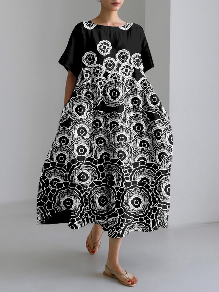 a woman in a black and white floral dress stands on a white background. she is wearing sandals.