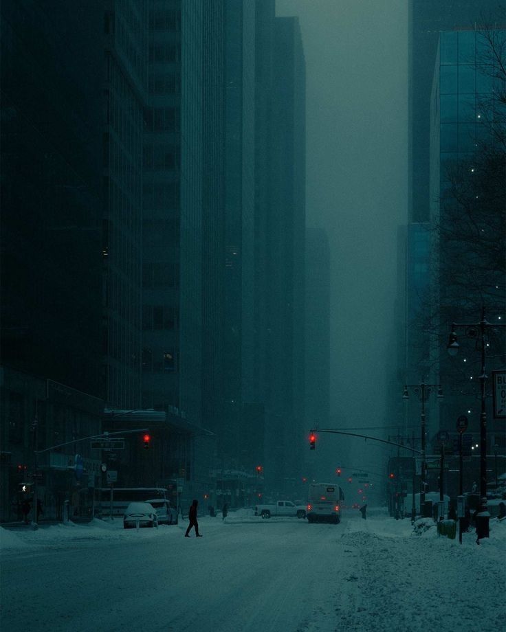 the image depicts a snowcovered street in a city, possibly new york city, at night during a snowstorm. tall skyscrapers flank the street, which is mostly empty except for a solitary pedestrian walking and a few vehicles. the atmosphere is dark, moody, and atmospheric, with a heavy fog or mist reducing visibility. the streetlights and red traffic lights add to the bleak and cold ambiance. the overall color palette is a muted teal or cyan. the scene is quiet and solitary, emphasizing a sense of isolation and calm within the urban environment.