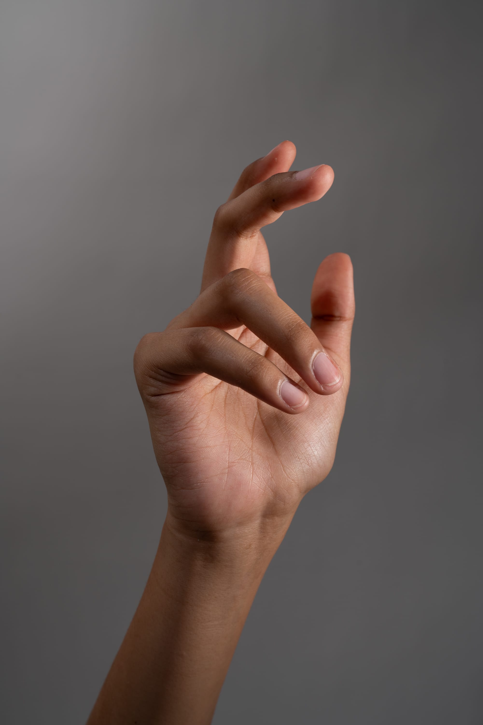 a hand is shown against a gray background. the hand is making a gesture with the thumb and index finger touching, while the other fingers are slightly curled. the image is well lit, suggesting studio lighting.