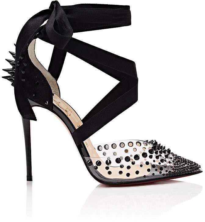 a pair of christian louboutin high heels are shown.  the shoes are black and clear, with a transparent toe and heel.  the shoes are studded with black spikes, and have a black ribbon ankle strap that ties in a bow. the shoes are elegant and stylish, and are perfect for a special occasion.  they have a stiletto heel. the image shows the shoes on a white background, and there is a reflection of the shoes below.