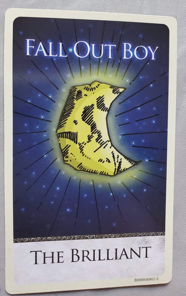 a fall out boy album cover featuring a crescent moon with black outlines and yellow shading. the background is a navy blue color with a white rim and a white "fall out boy" and "the brilliant" written in black. the bottom right corner has a small white rectangle with a black text that says "b000s40802e."