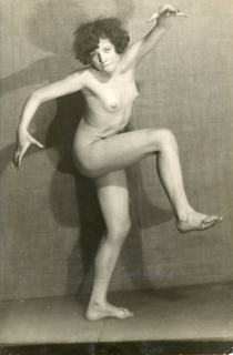 a black and white photograph of a nude woman in a dynamic pose.  she is positioned slightly offcenter, her body angled, with one leg raised. her dark hair is short and wavy.  the background is a textured wall, providing contrast to her body. the photo appears to be from the early to mid 20th century, possibly the 1920s or 1930s, and possesses a distinctly artistic style suggesting movement and expressionism.  the lighting accentuates her form and creates shadows which add depth to the image.