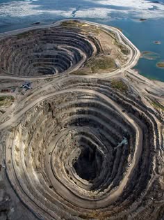 an aerial shot of a massive diamond mine in a crater shaped like a large bowl with layered earth formations.  the depth of the mine is evident and the rock formations look like stripes.  the surface of the mine and the surrounding area are covered with vegetation, a sign of natural rejuvenation.  the image was taken from above and captures the vastness and beauty of the mine.