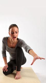 a woman in workout attire is performing a yoga pose on a tan surface. she's leaning forward and reaching out with her right arm while looking forward with her mouth open.