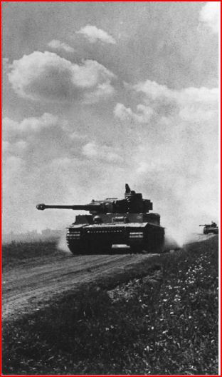 a black and white photograph depicting a german tiger tank (panzerkampfwagen vi tiger) moving across a flat, open landscape. the tank is the main focus of the image, occupying a significant portion of the frame.  a second, smaller tank is visible in the distance to the right. the sky is partly cloudy. the overall scene suggests a wartime setting, potentially during a military operation.  the image has a grainy texture characteristic of older photographs.