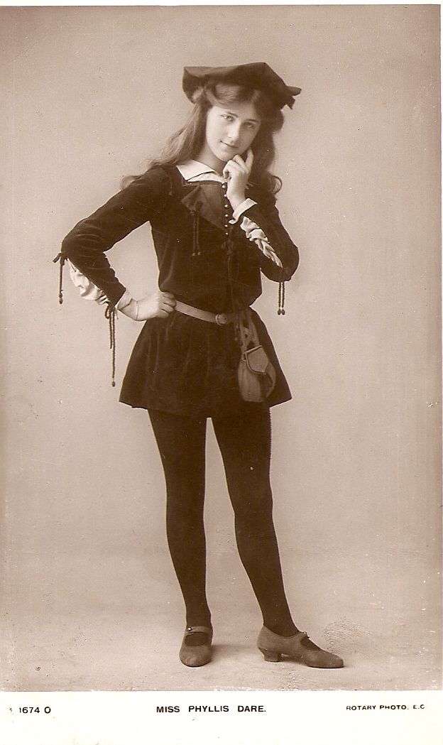 a fullbody vintage sepia photograph shows miss phyllis dare standing in a threequarter pose. she is wearing a period costume consisting of a dark dress or tunic with a lightercolored collar and cuffs, dark tights, and shoes with a strap. a pouch hangs from a belt at her waist, and she has a small, soft hat perched on her head. her right hand is raised to her chin in a pensive gesture. the background is plain. the words "miss phyllis dare" are printed below the image.
