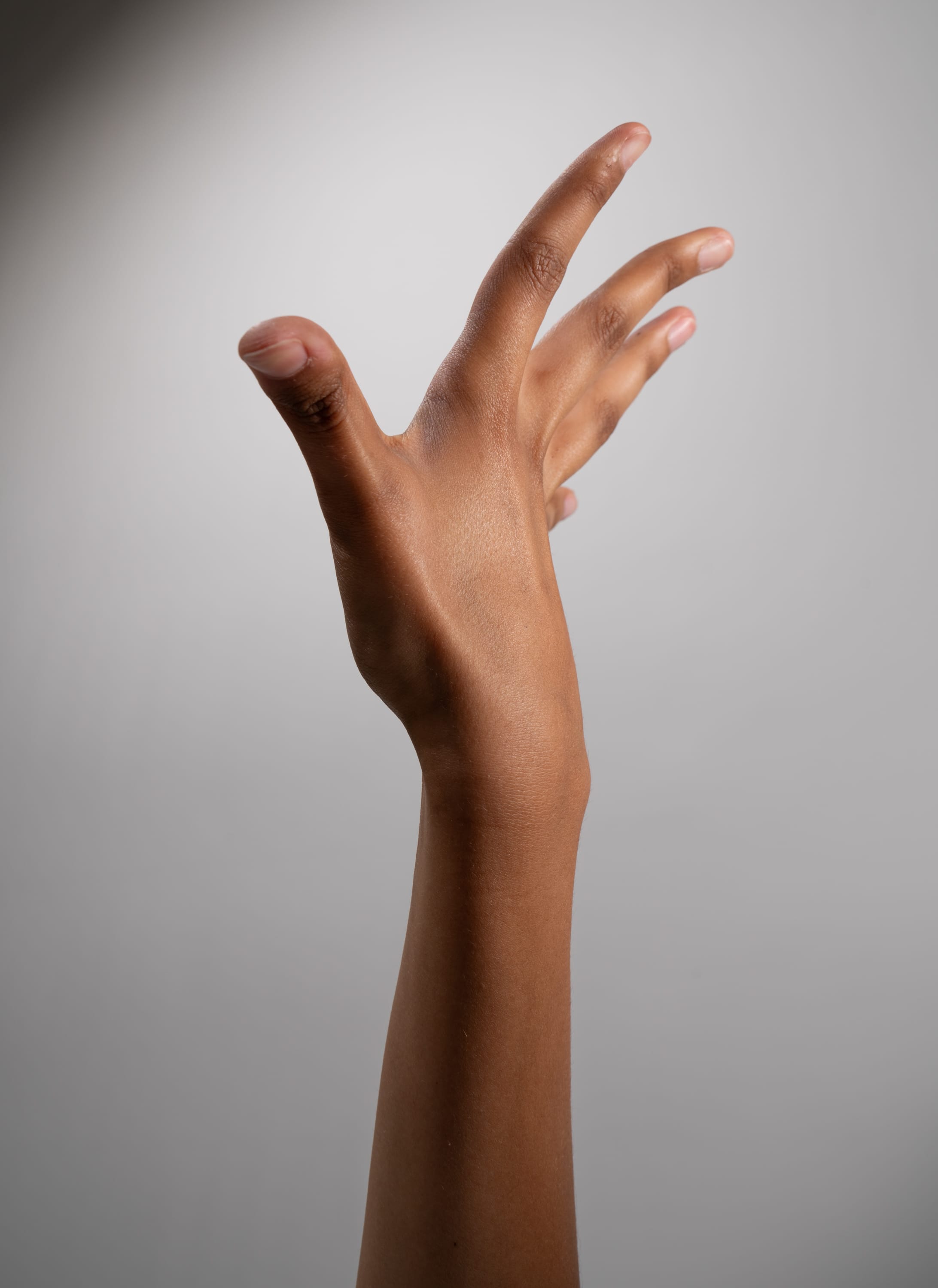 the image shows a hand reaching up with an open palm against a gray background. the hand belongs to a person with dark skin. the light in the image appears to be artificial studio lighting.