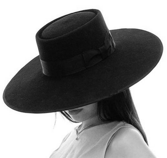 a woman in a black fedora hat with a wide brim is photographed in black and white.  her face is mostly hidden under the brim of the hat.  she appears to be looking down and to the left.