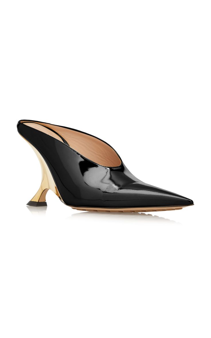 a pair of black patent leather mules with a gold stiletto heel is shown. the shoes are pointedtoe and have a unique heel design. they appear to be highend, designer shoes.  the image is a product shot, likely for an online store or catalog.