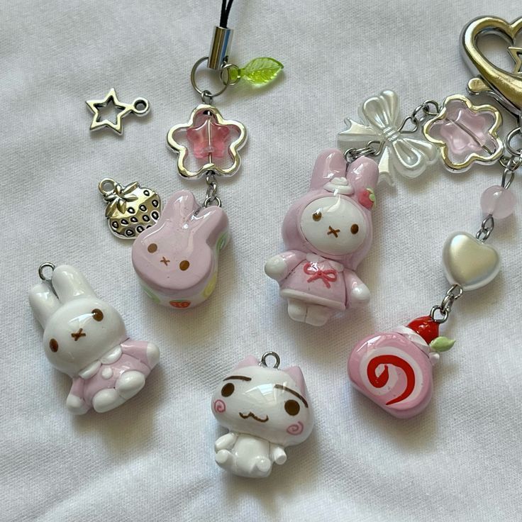 the image shows a collection of kawaii charms arranged on a white fabric surface. there are several sanriothemed charms including my melody and bunny shapes, along with a cat charm. other charms include a star, strawberryshaped item, and a roll cake charm. the charms are made in pastel colors and are part of a keychain or a collection of cute accessories.