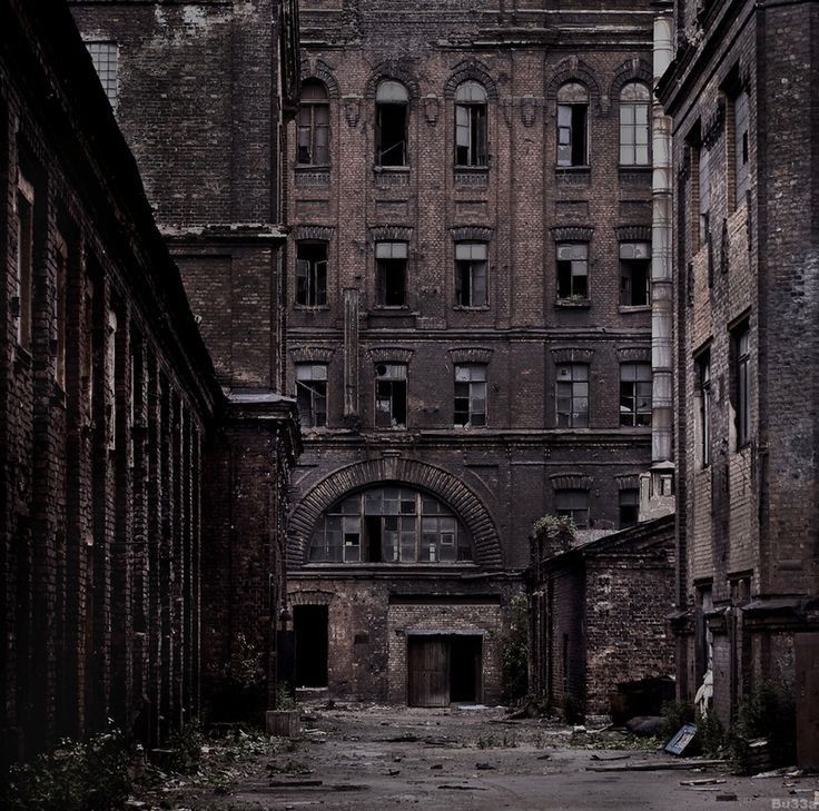 the image depicts a desolate, abandoned industrial area.  the scene is dominated by aged brick buildings, many with broken windows and doors. a narrow alleyway or courtyard leads the eye towards a large brick structure that appears to be a former factory or warehouse. the overall mood is dark, gloomy, and suggestive of urban decay, with a strong sense of abandonment and a somewhat haunting atmosphere. the color palette is muted and dark, enhancing the overall sense of age and desolation.