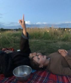 a couple is laying down on a blanket in a grassy field under the night sky. the