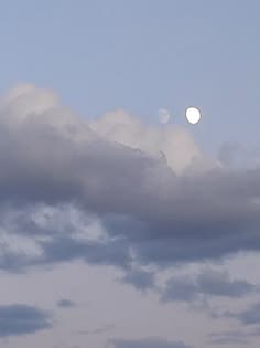a bright, white moon is visible in the middle of the picture, surrounded by fluffy white clouds, which cover the entire sky.  the sky is a light blue color.